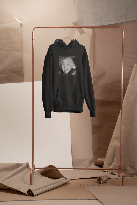 Black hoodie hanging on a copper clothing rack, featuring a black-and-white image of Albert Einstein playfully sticking out his tongue. The background includes neutral-toned paper and fabric drapes for a minimalist aesthetic.