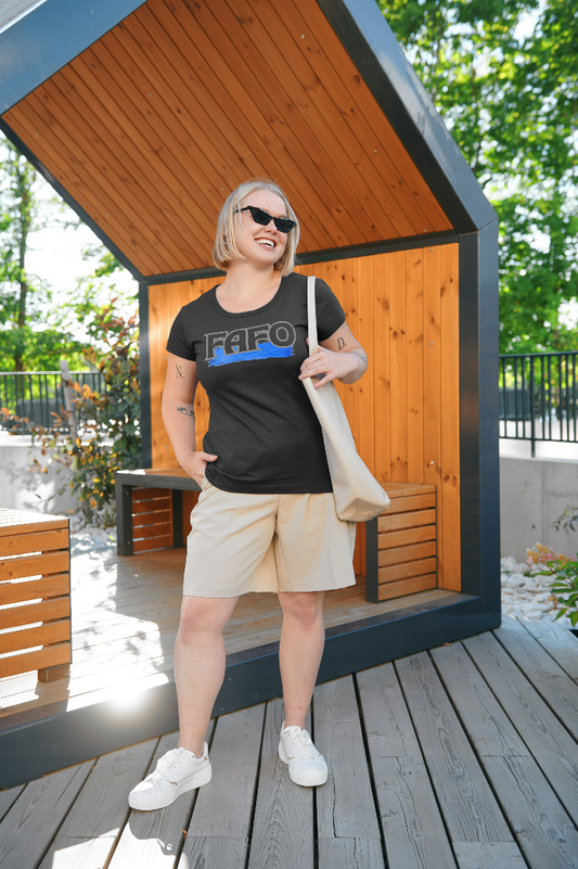 Person wearing a black t-shirt with "FAFO" printed in bold letters, featuring a distressed blue strike-through effect. They are outdoors, smiling confidently, with casual shorts, white sneakers, and sunglasses.